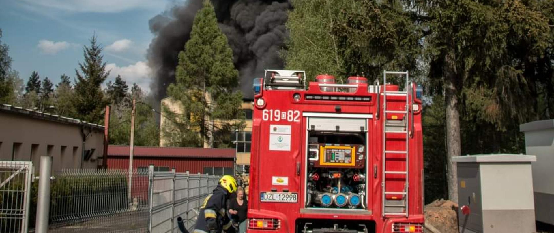 tył samochodu pożarniczego z podłączonymi liniami gaśniczymi, w tle słup czarnego dymu