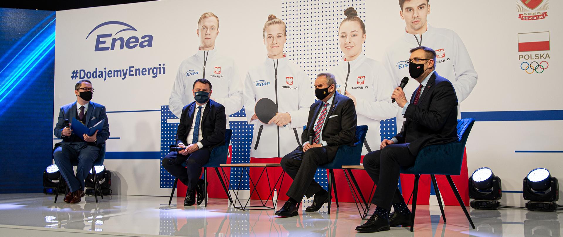 Konferencja Grupy Enea poświęcona wsparciu dla PKOL. Na scenie siedzą paneliści. W tle ścianka z logo PKOL i wizerunkami sportowców