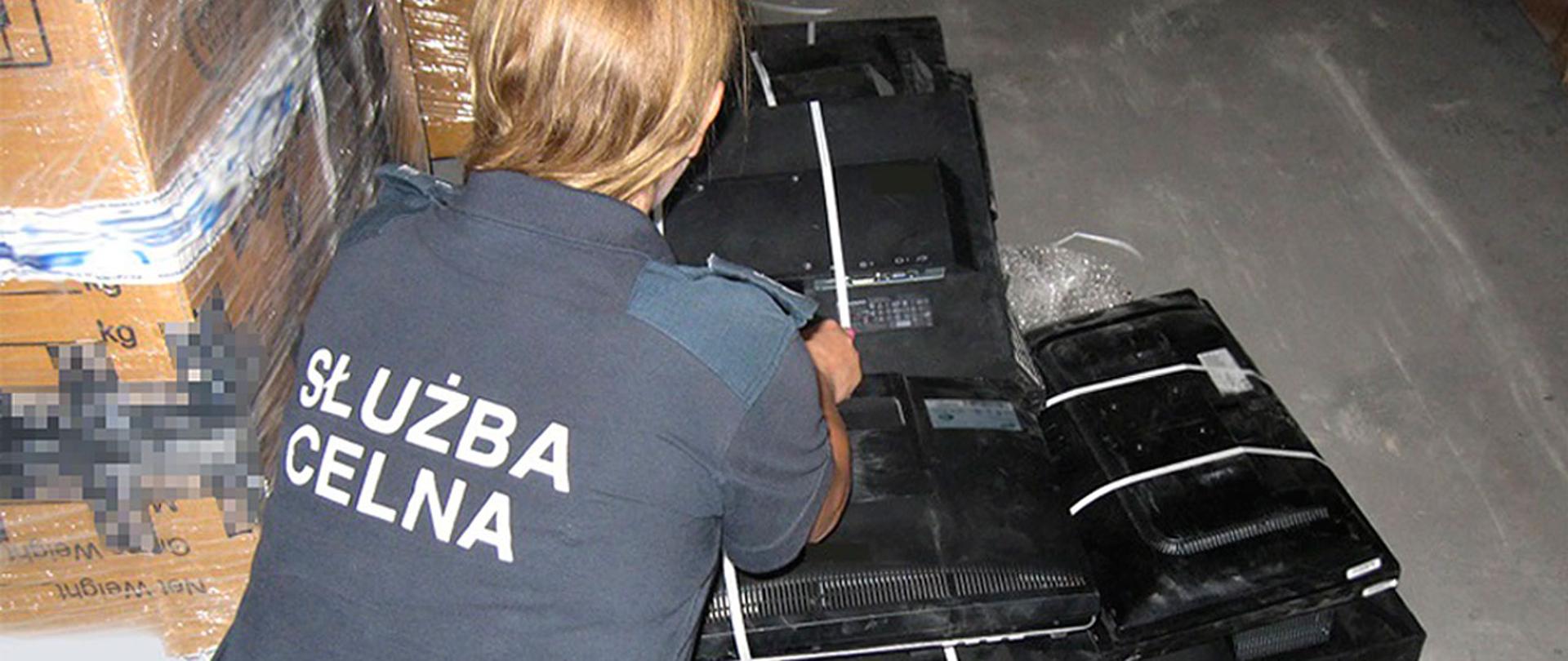 Funkcjonariuszka Służby Celno-Skarbowej przy rozłożonych na podłodze używanych monitorach komputerowych