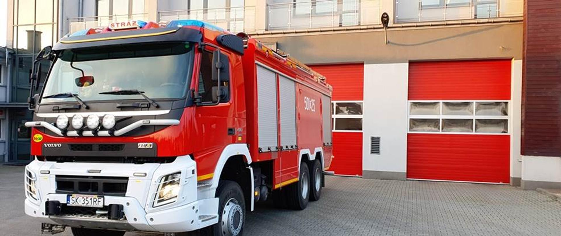 Samochód pożarniczy na tle bram garażowych.