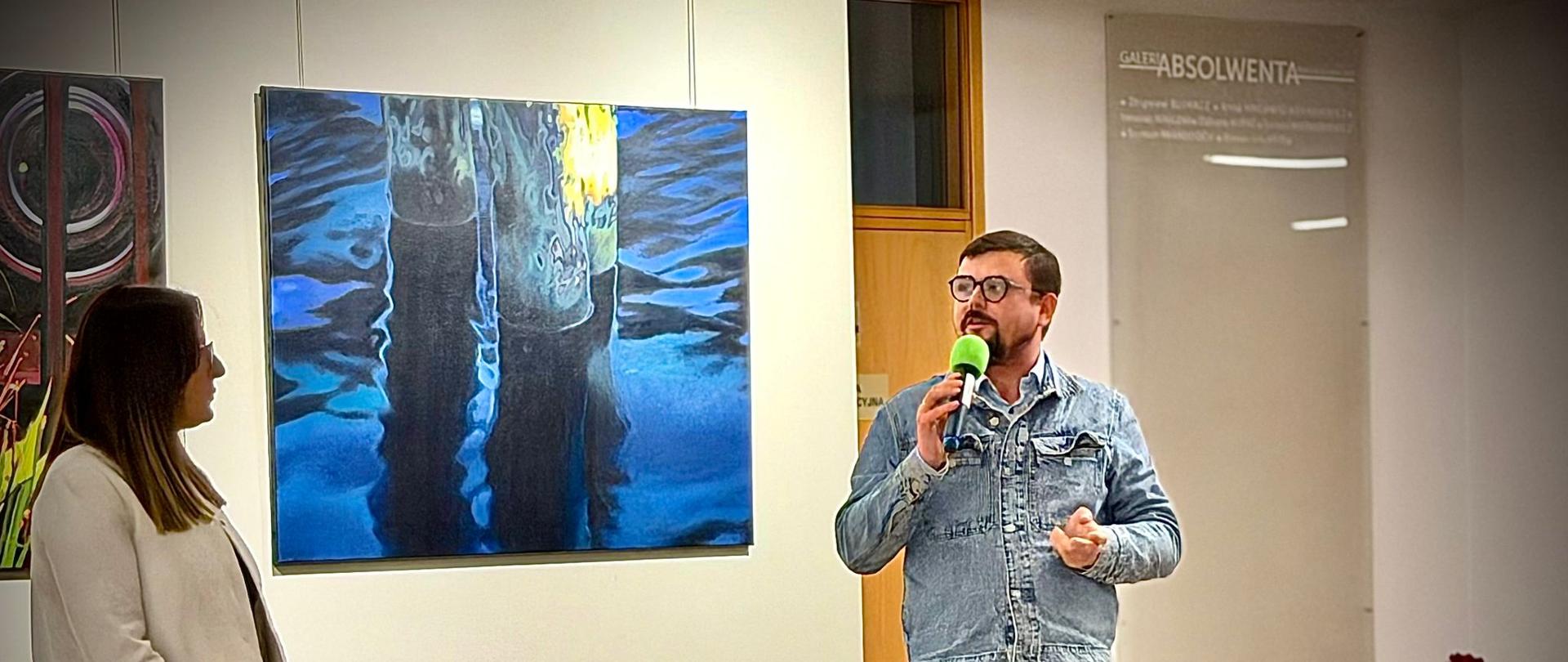 Fotografia ukazująca Wicedyrektor Aleksandrę Klimas oraz Pawła Słotę na tle obrazów artysty.