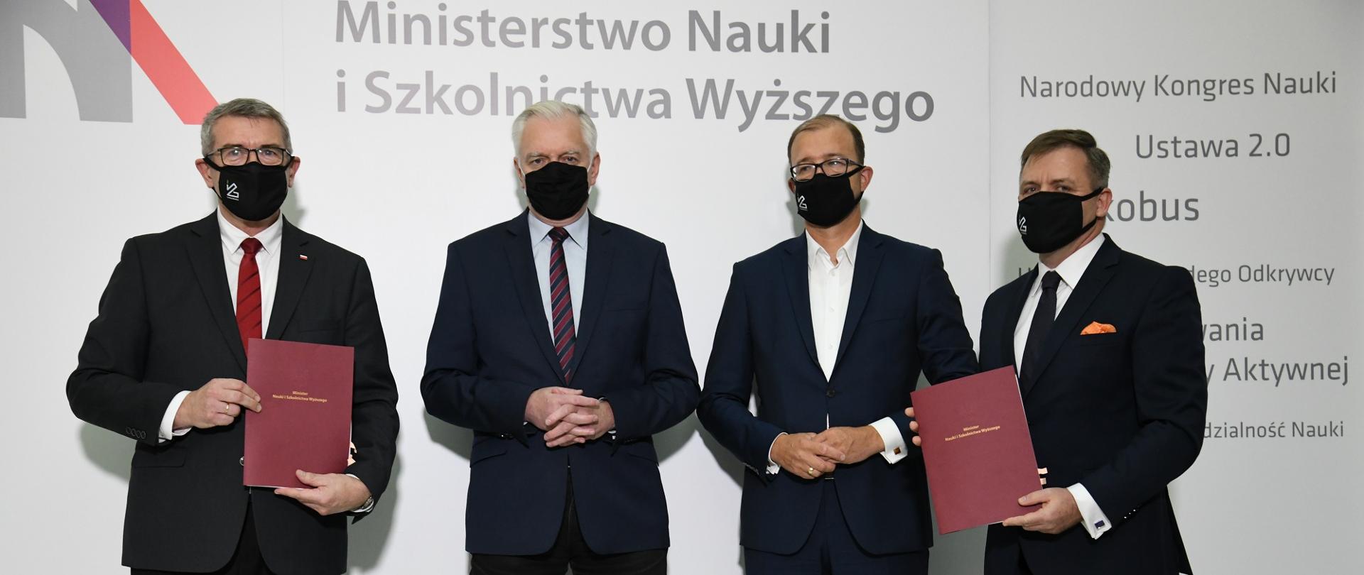 Uczestnicy spotkania w maseczkach stoją przed ścianą z logiem MNiSW.