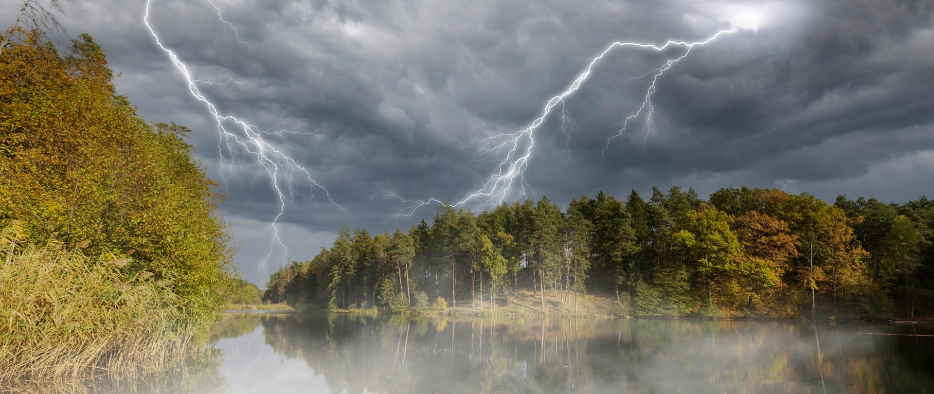 Zdjęcie przedstawia jezioro wśród drzew nad którym panuje burza z błyskawicami.
