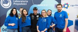 Przed niebieską ścianką z napisem Laboratoria przyszłości stoi grupa uśmiechniętych młodych osób w niebieskich bluzach.