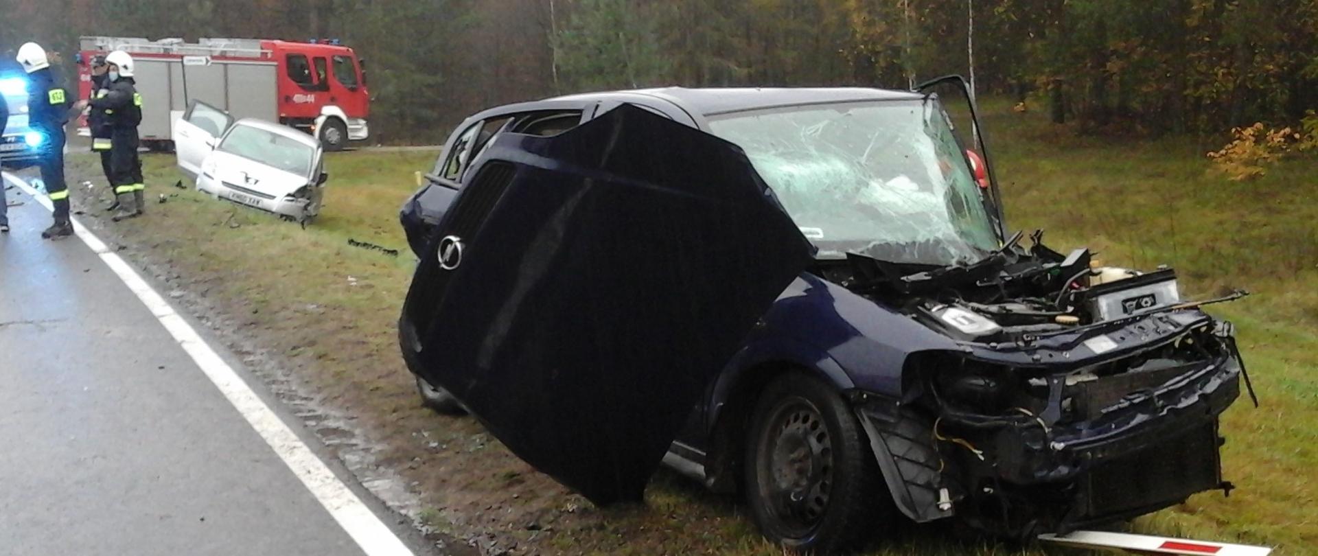 Zdjęcie wykonane podczas działań ratowniczych na DK-19 w Deniskach. Widok na rozbite pojazdy. W tle samochód pożarniczy.