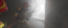 Zdjęcie przedstawia strażaków, którzy podają wodę na palące się pomieszczenia w budynku gospodarczym. 