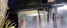 Pora nocna, spalony murowany budynek sauny ogrodowej. Nad nim widać spaloną konstrukcję dachu. 