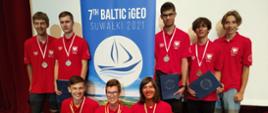 Grupa ludzi w koszulkach reprezentacji Polski. Na środku rollup Bałtyckiej Olimpiady Geograficznej