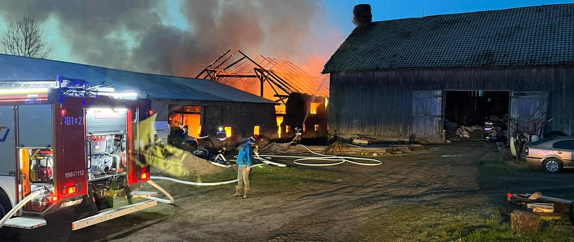 Zdjęcie przedstawia budynek gospodarczy w płomieniach oraz zagrożoną bezpośrednio stodołę.