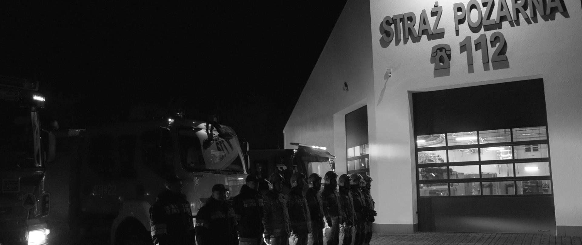 Strażacy ustawieni w szeregu stoją przed budynkiem Komendy Powiatowej PSP w Golubiu-Dobrzyniu. Za nimi widać wozy bojowe.
