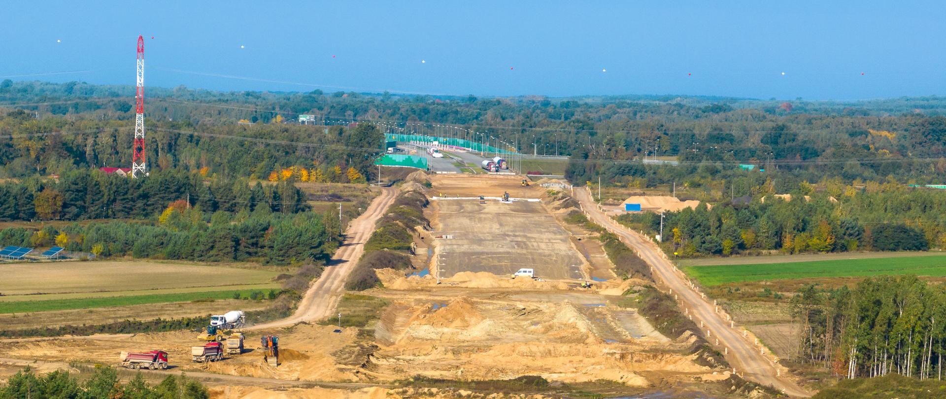 Widok na plac budowy autostrady A2. Wczesny etap prac. Widoczny szeroki pas oczyszczonej ziemi i przygotowanej podbudowy pod nową autostradę. W tle, na horyzoncie widoczne już gotowe pasy ruchu.