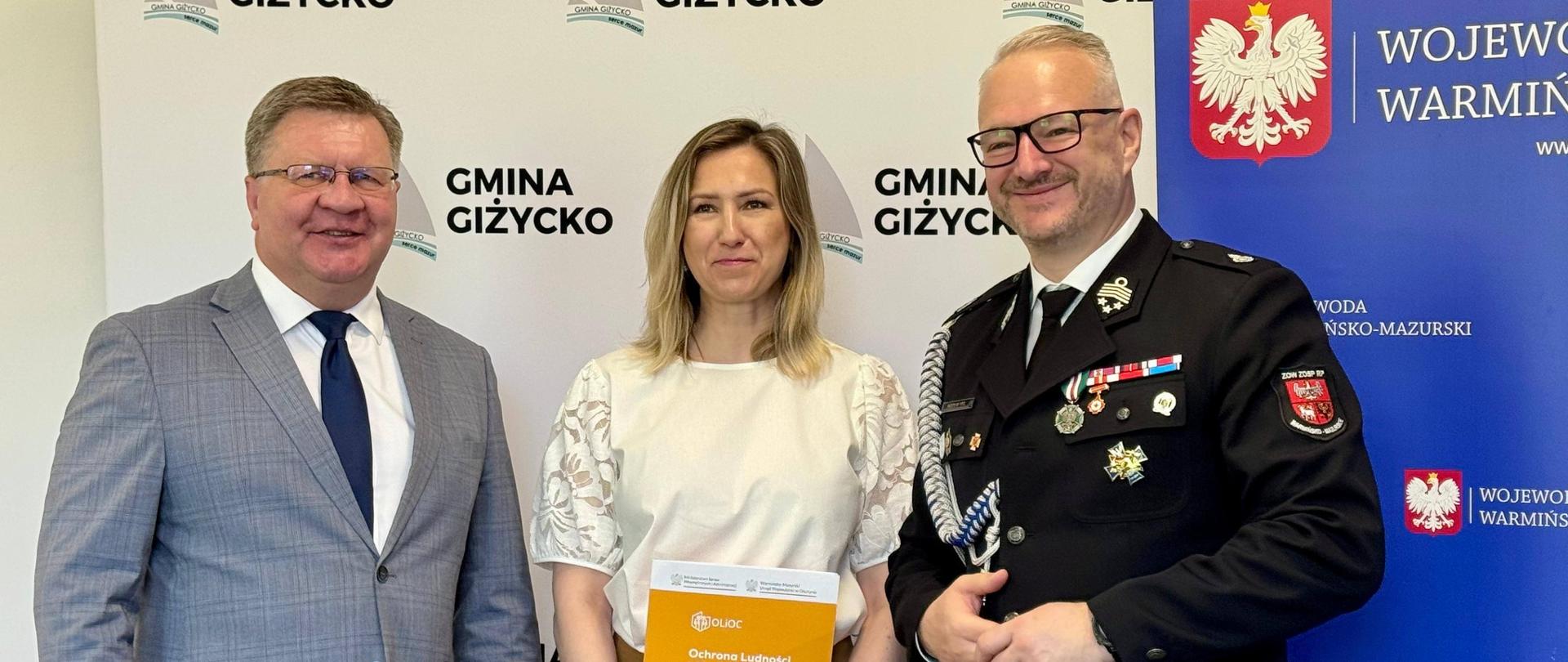 grupa oficjeli, w tym wojewoda, pozują do zdjęcia na tle ścianki 