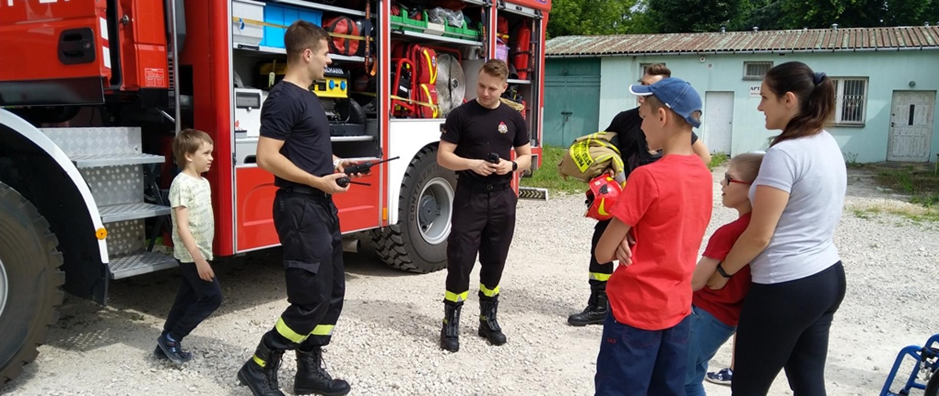 Na zdjęciu samochód pożarniczy z otwartymi skrytkami sprzętowymi, strażacy prezentujący sprzęt będący na wyposażeniu samochodu, w pokazie uczestniczą dzieci z Ośrodka Edukacyjno-Rehabilitacyjnego „Kolorowa Skarpetka” we Włoszczowie