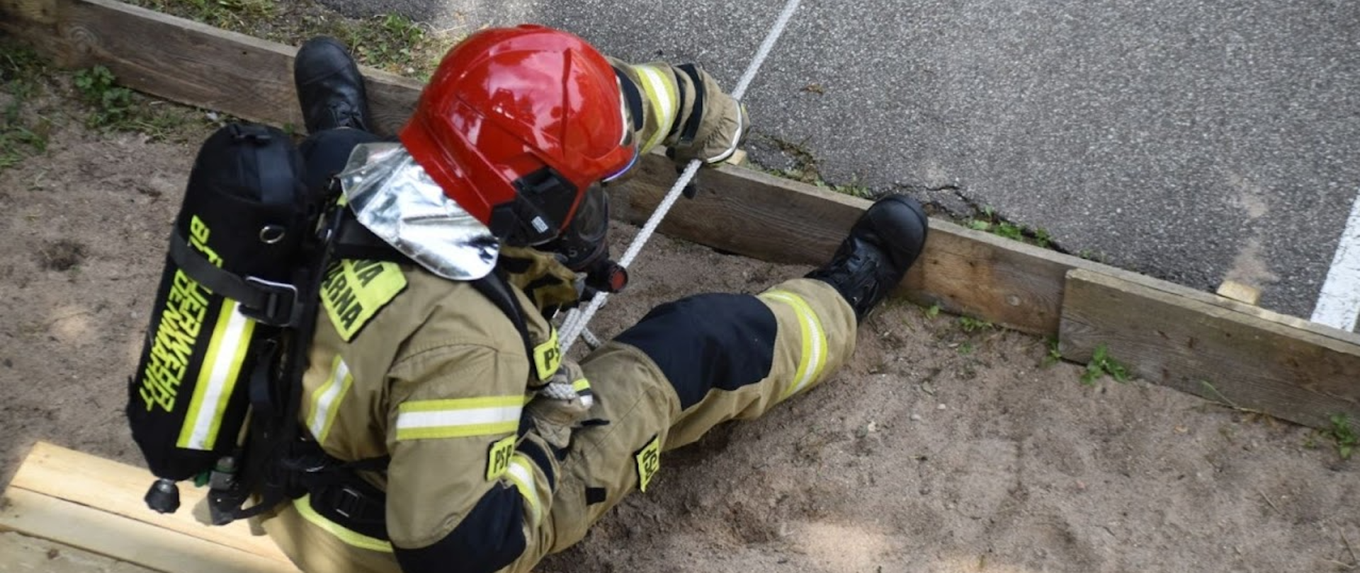 Strażak siedzący w ubraniu specjalnym na ziemi i siągnący linę z oponą