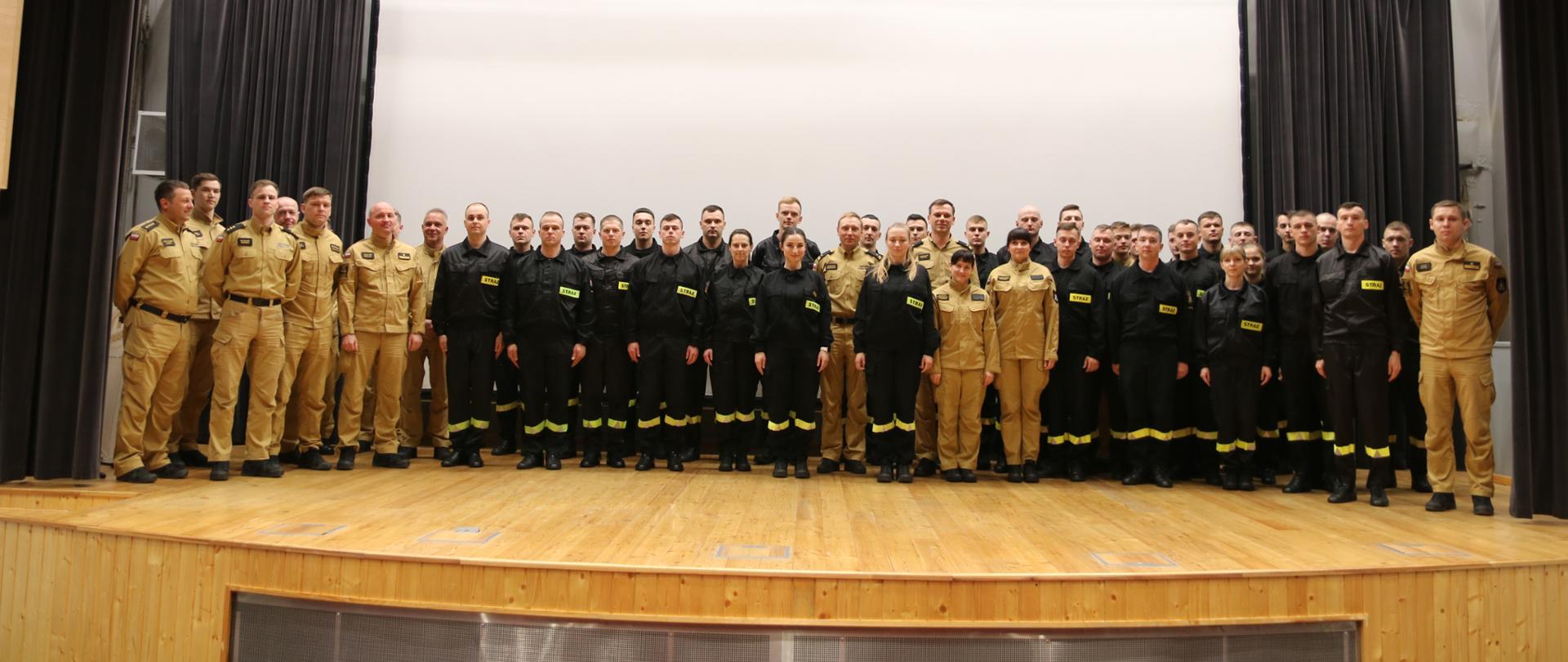 Pamiątkowe zdjęcie uczestników zbiórki. Strażacy stojący na scenie auli SA PSP w Krakowie 