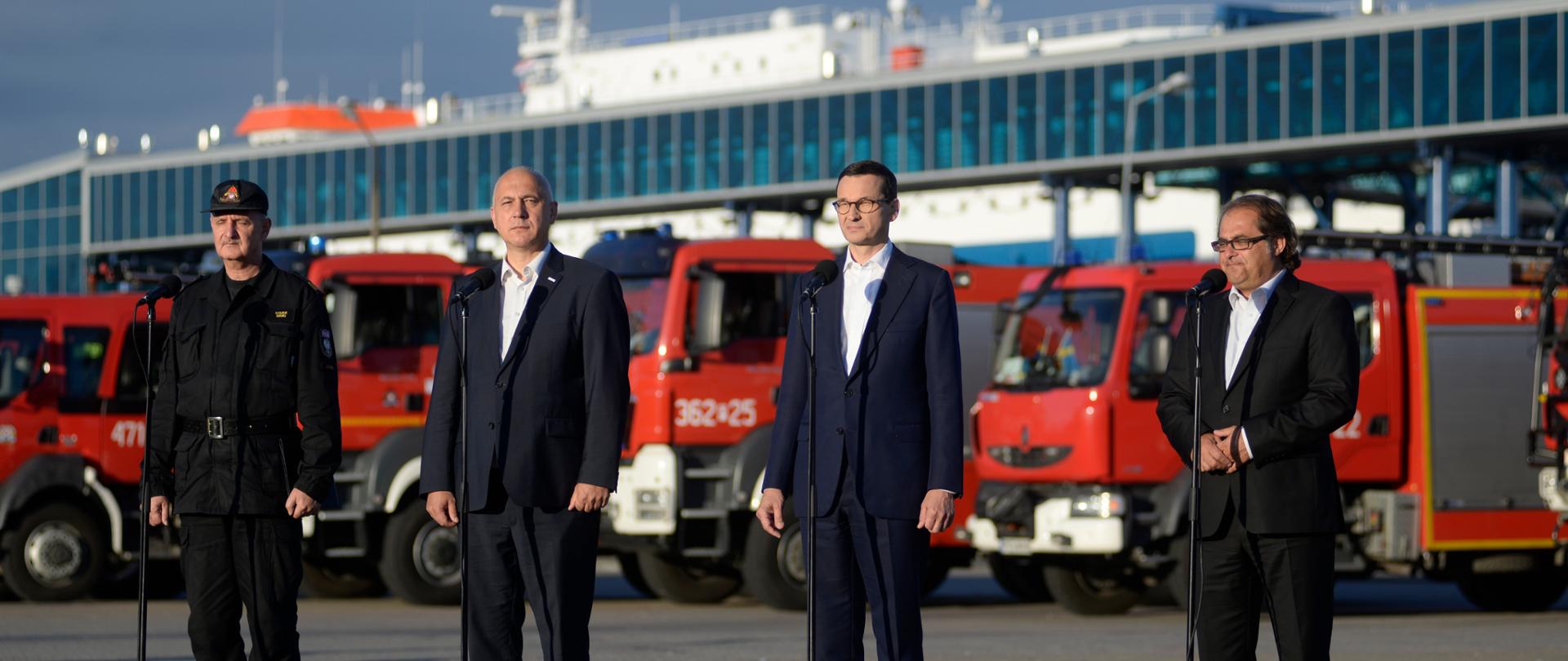 Premier Mateusz Morawiecki wraz z ministrem Markiem Gróbarczykiem oraz ministrem Joachimem Brudzińskim przemawiają podczas ceremonii powitania polskich strażaków wracających ze Szwecji. 