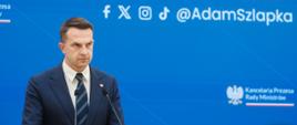Rzecznik rządu, Minister Adam Szłapka podczas konferencji prasowej 24.06.2025 r. W tle ekran Kancelarii Prezesa Rady Ministrów oraz media społecznościowe rzecznika rządu. 