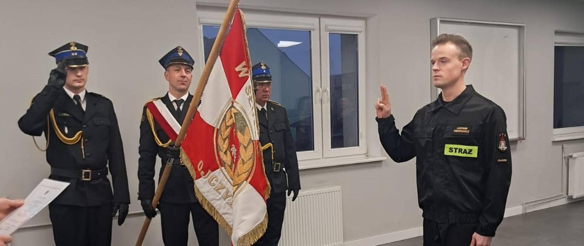 Po lewej stronie stoi poczet sztandarowy KP PSP w Człuchowie podczas uroczystości składania ślubowania przez str. Jaromira Kiedrowicza stojącego po prawej stronie.