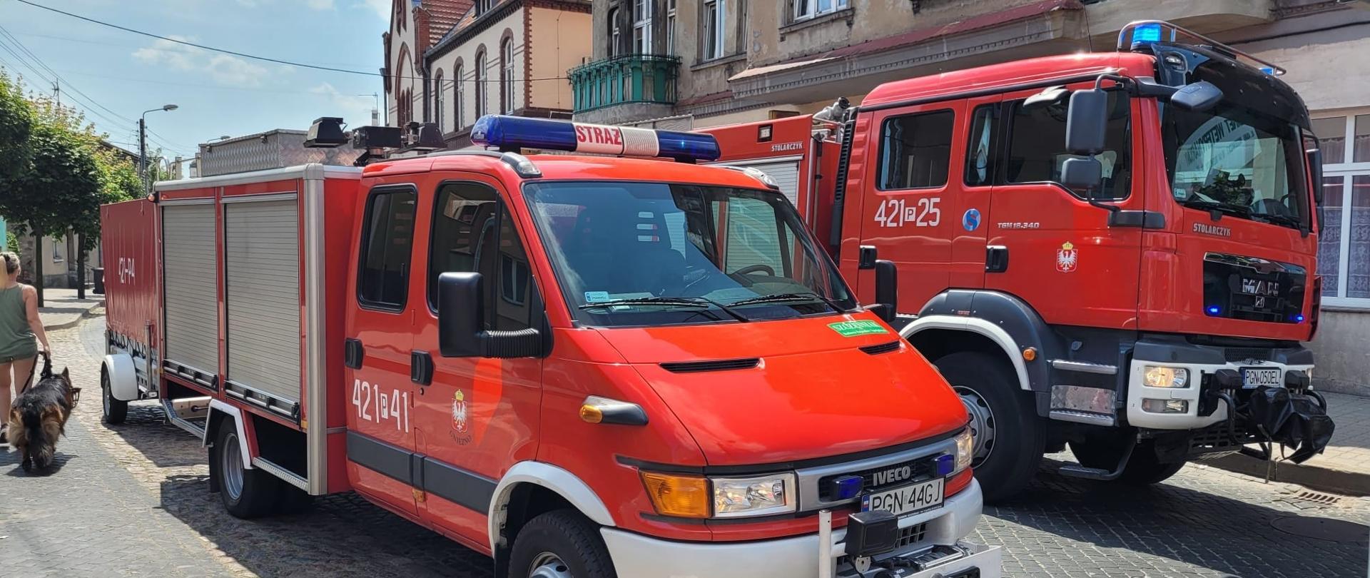 Czerwone samochody strażackie stoją na jezdni z ciemnej kostki brukowej obok siebie 