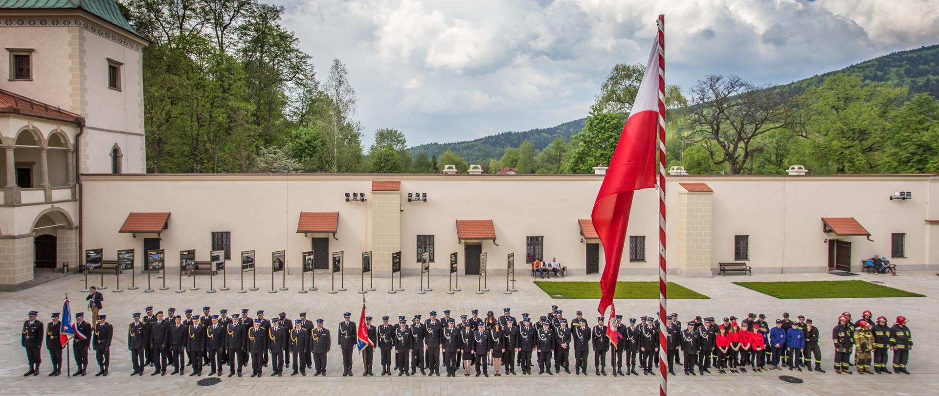 Zdjęcie przedstawia zbiórkę pododdziałów Państwowej Straży Pożarnej oraz Ochotniczej Straży Pożarnej na dziedzińcu zamku suskiego. 