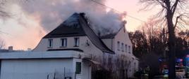 Na zdjęciu widać palący się budynek mieszkalny, z dachu wydobywa się duża ilość dymu.