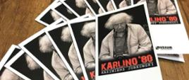 Na centralnym punkcie zdjęcia kilka ulotek promocyjnych odnośnie wystawy. Każda z ulotek przedstawia autora galerii. Ulotka czarno-biała z czerwonym napisem Karlino