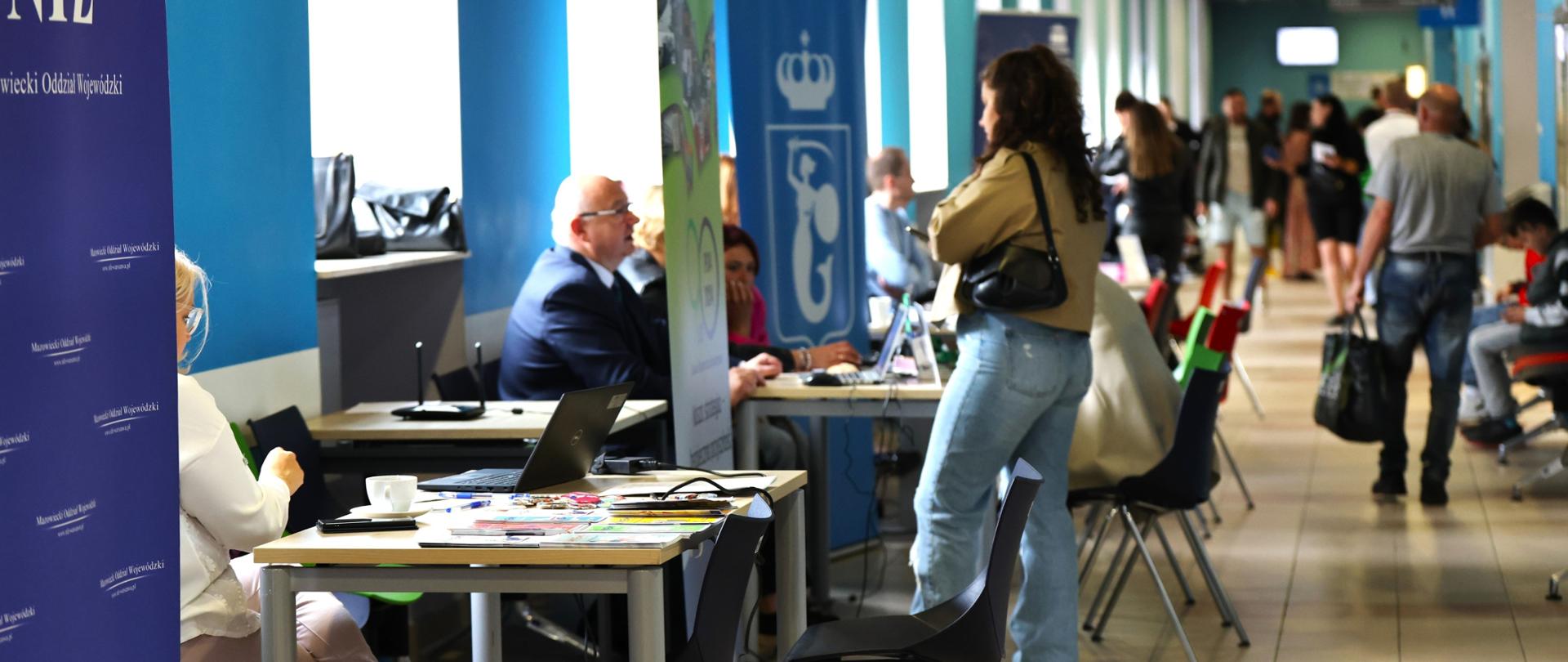 tłum ludzi zebrany na korytarzu wydziału, część osób siedzi przy stolikach ustawionych pod oknami