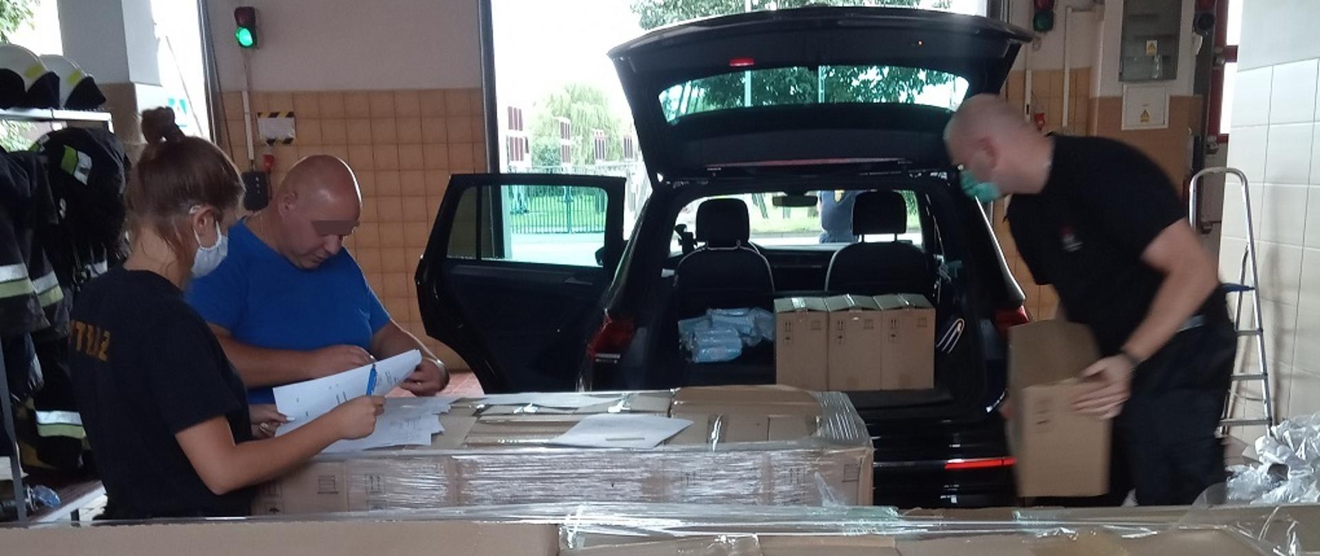 Strażacy przekazujący środki ochrony indywidualnej w kartonach z Agencji Rezerw Materiałowych dla uczniów i nauczycieli w szkołach powiatu lęborskiego.