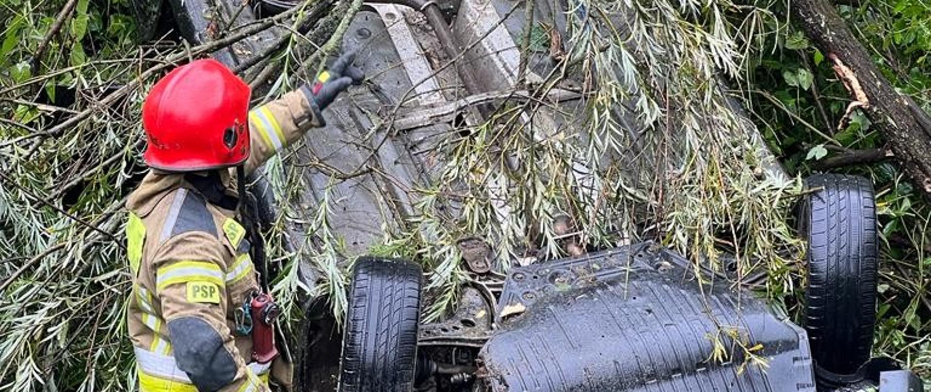 Samochód osobowy na dachu a obok strażak