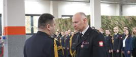 Komendant Wojewódzki gratuluje Komendantowi Miejskiemu, w tle inni strażacy.
