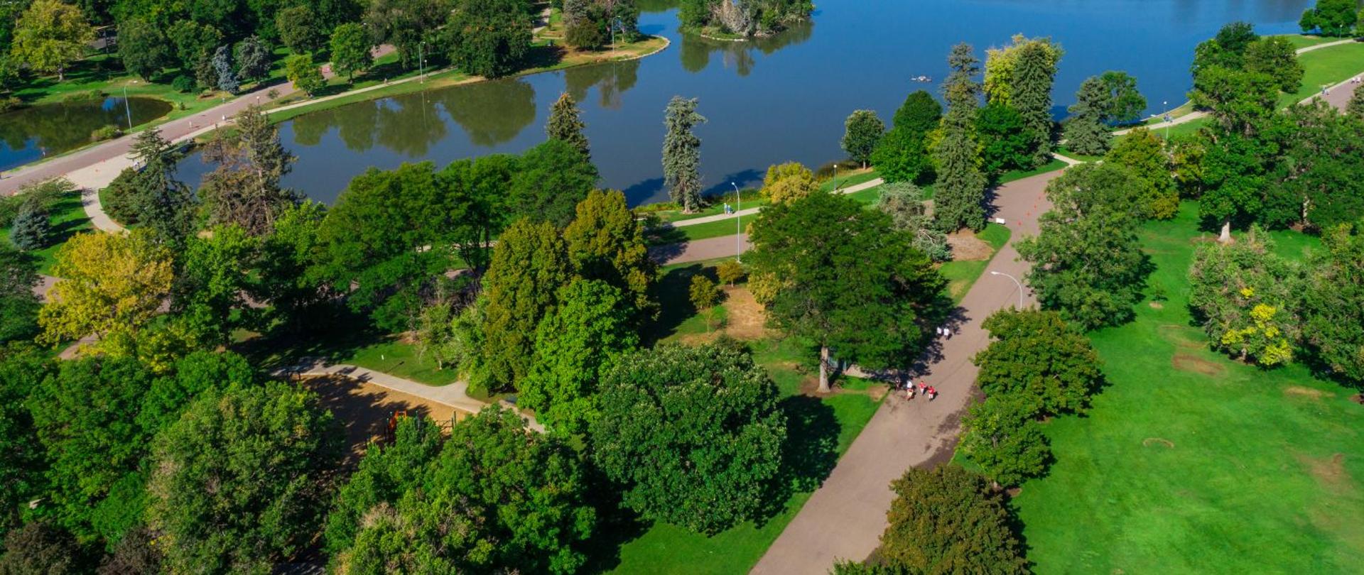 Na zdjęciu przedstawiony jest park miejski z lotu ptak. Znajdują się alejki dla spacerowiczów oraz niewielki staw