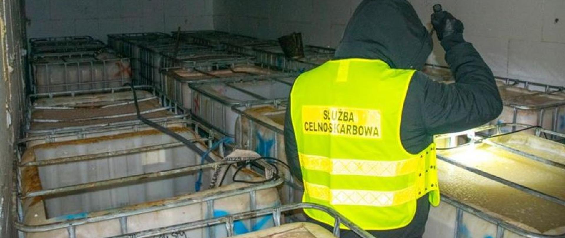 Funkcjonariusz Służby Celno-Skarbowej podświetla latarką mauzery wypełnione brudną cieczą