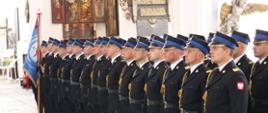 Kompania strażacka stoi na baczność ze sztandarem w kościele.