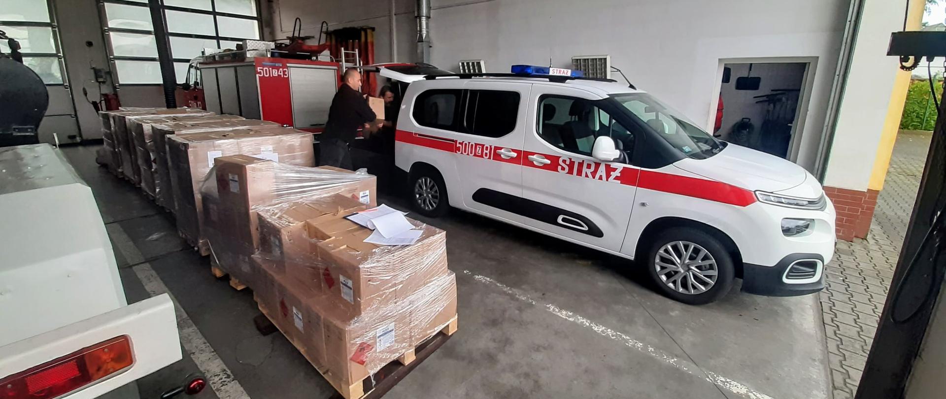 Dużo kartonów na paletach na garażu obok samochodów straży pożarnej