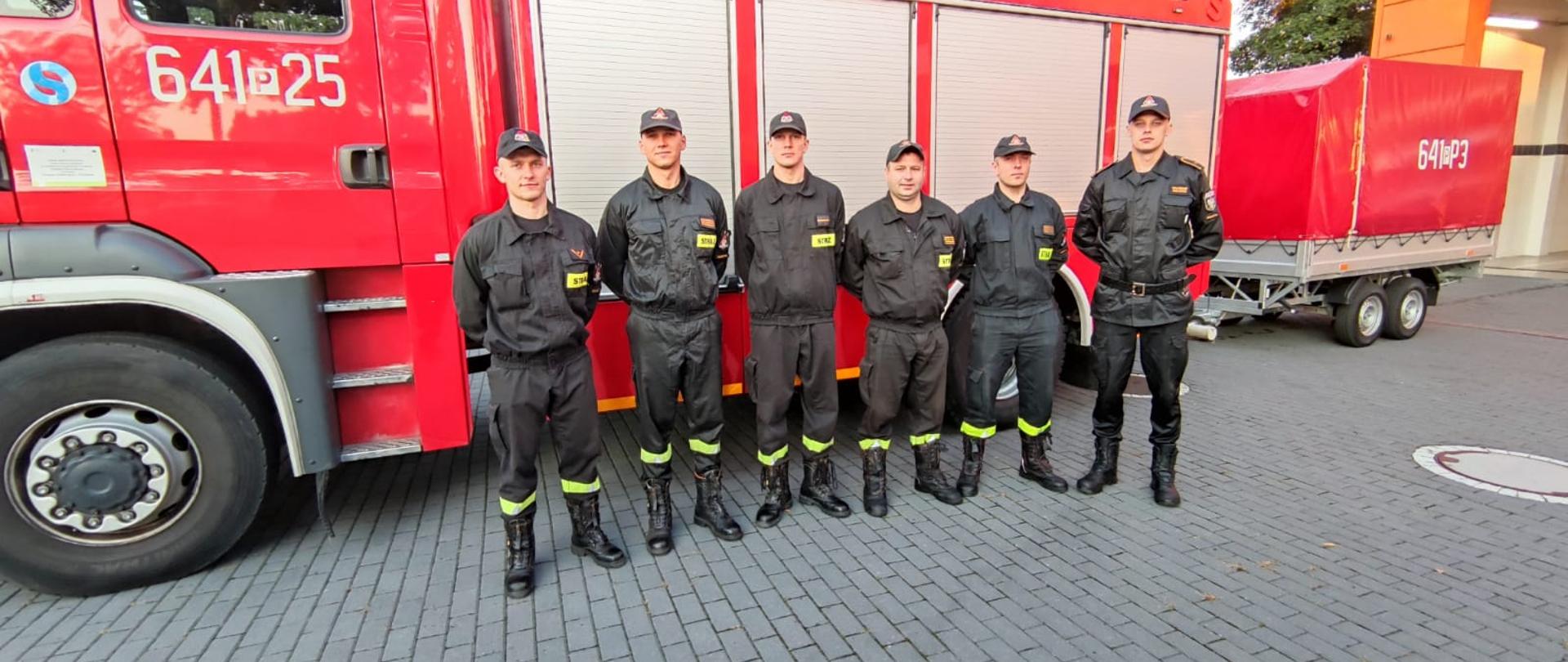 Strażacy stoją przy wozie gaśniczym