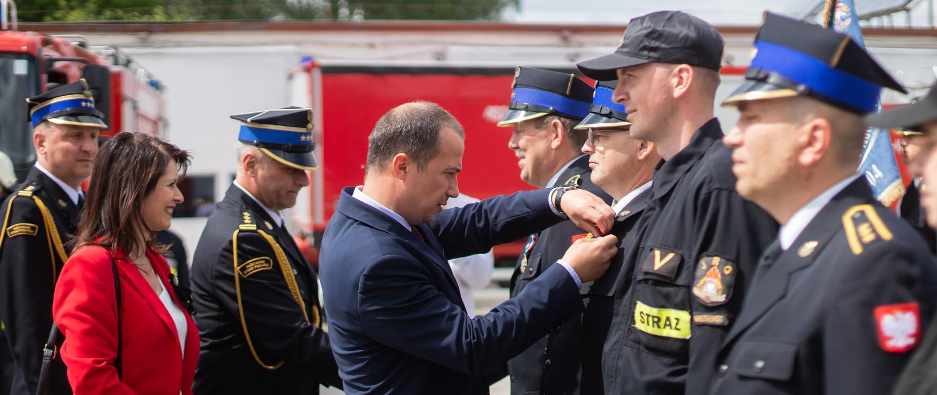 
Tłum ludzi – w strażackich mundurach i garniturach - stojący przed remizą
