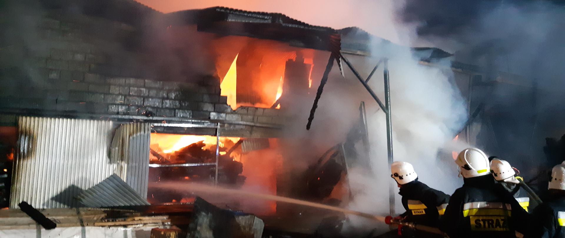 Zdjęcie przedstawia czterech strażaków gaszących pożar stolarni 