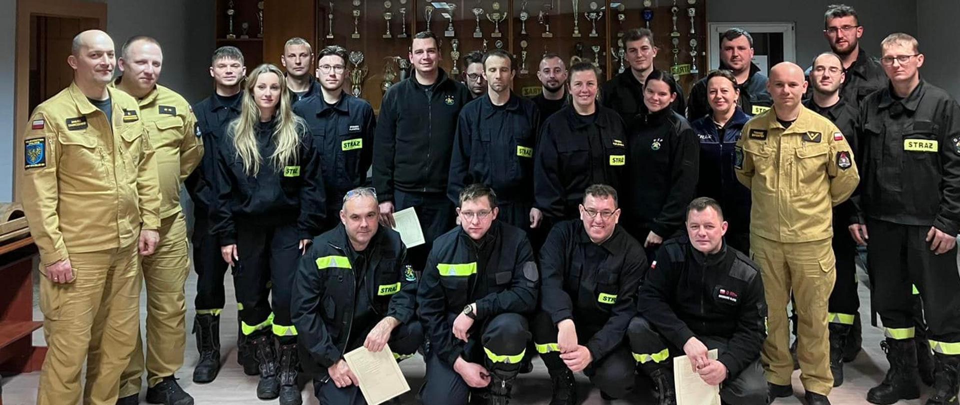 Na zdjęciu znajdują się strażacy ubrani w ubrania koszarowe ustawieni do zdjęcia w sali wykładowej