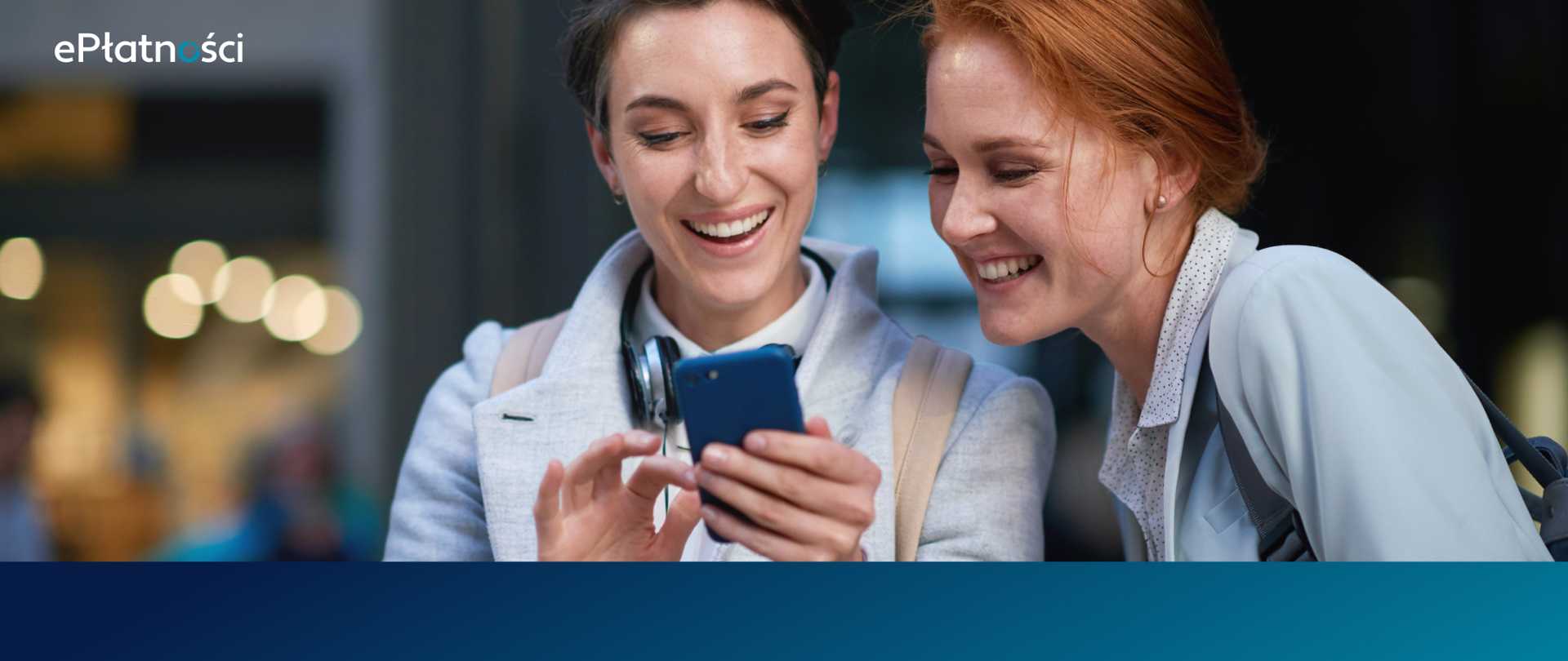Dwie uśmiechnięte dziewczyny patrzą w telefon, który trzyma jedna z nich. Tło rozmazane, w lewym górnym rogu logo ePłatności