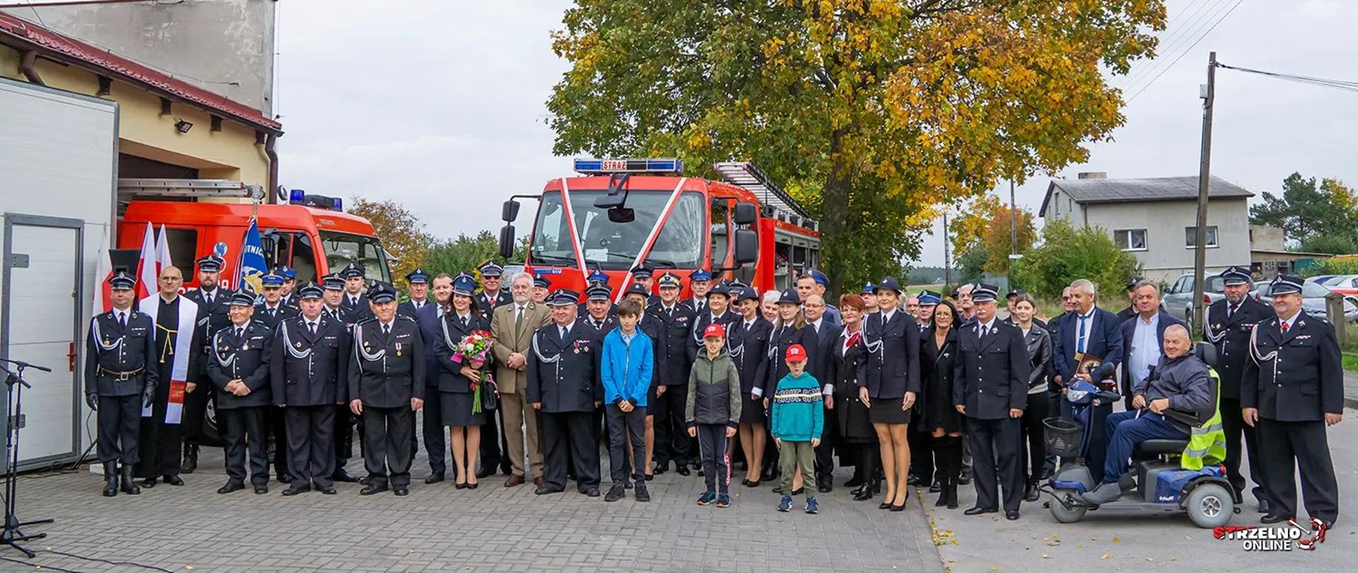 Druhowie i zaproszeni goście na tle przekazanego samochodu. Z garażu wystaje przód drugiego samochodu
