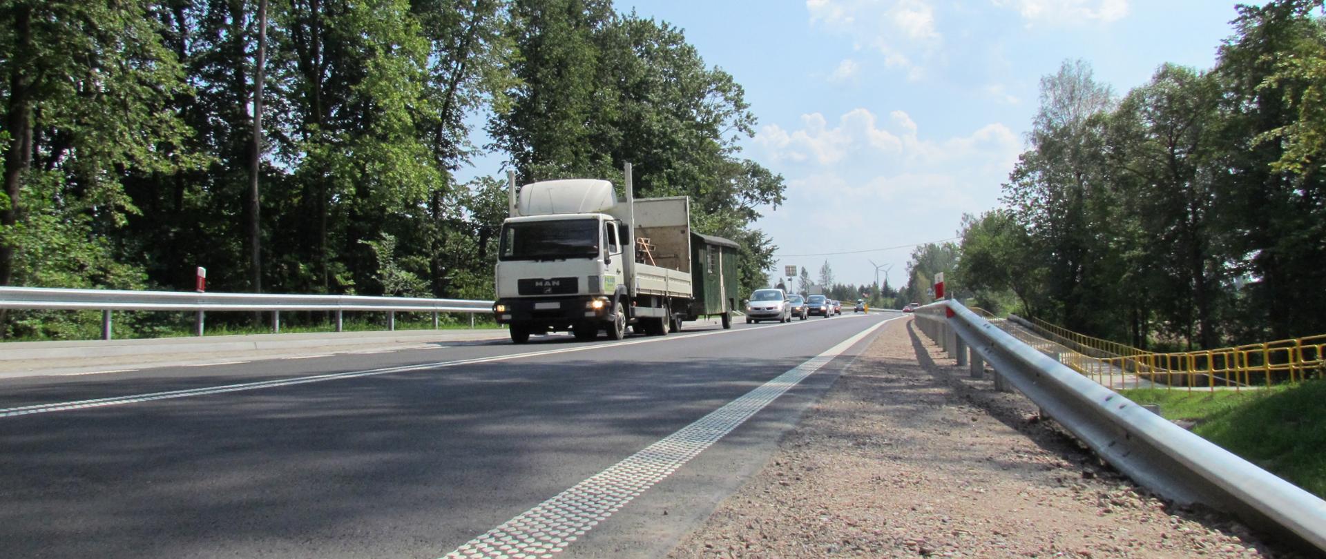 Asfaltowa droga wśród drzew. Na jednym z pasów sznur samochodów.