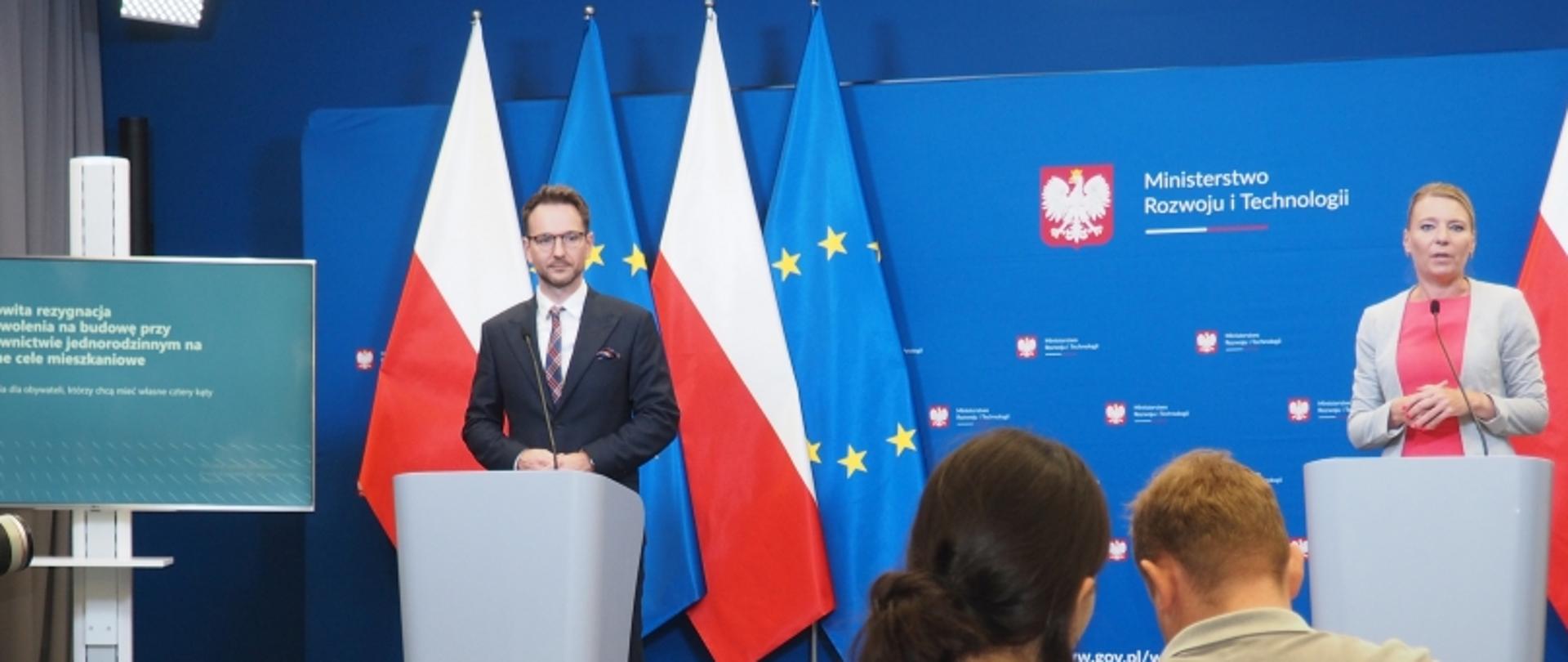 Dwóch prelegentów na konferencji prasowej Ministerstwa Rozwoju i Technologii, z flagami Polski i UE oraz ekranem z informacją o rezygnacji z pozwolenia na budowę.