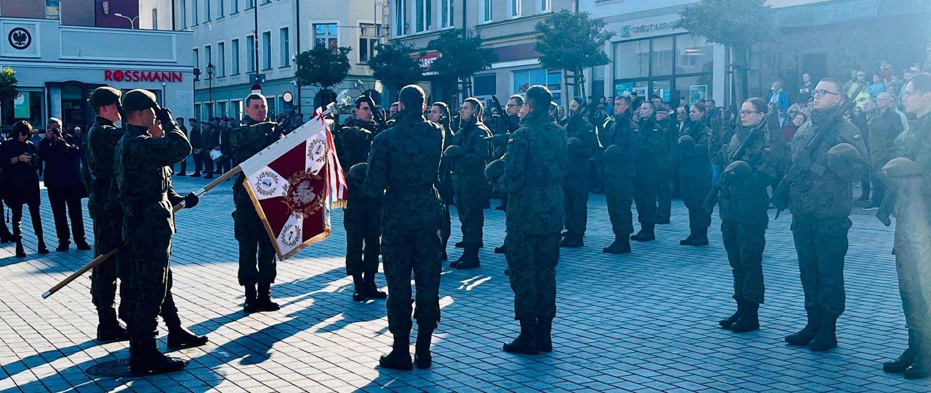 Zdjęcie przedstawia moment ślubowania. Widać umundurowanych żołnierzy 71 Batalionu Lekkiej Piechoty 7 Pomorskiej Brygady Obrony Terytorialnej, w tle budynki rynku miejskiego.