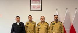 Awansowany strażak w towarzystwie przełożonych. z prawej strony wiszą flagi Polski. Na ścianie wisi godło Polski, 