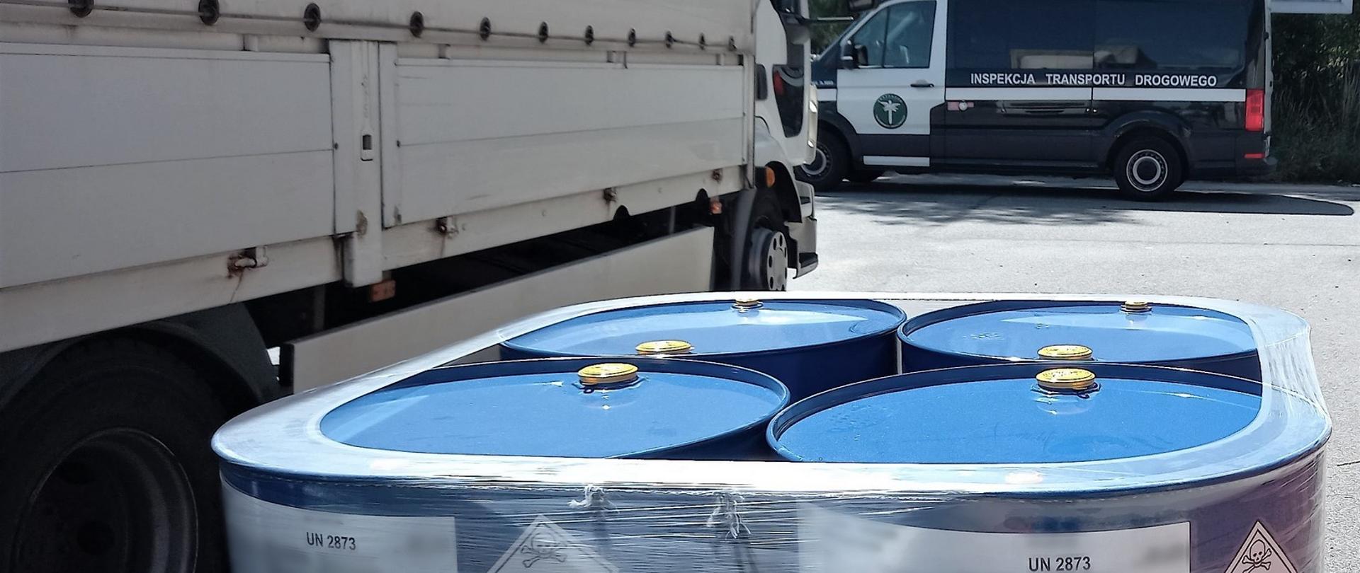 Na pierwszym planie: beczki z materiałem niebezpiecznym ADR i zatrzymana do kontroli ciężarówka. W tle: oznakowany furgon wielkopolskiej Inspekcji Transportu Drogowego.
