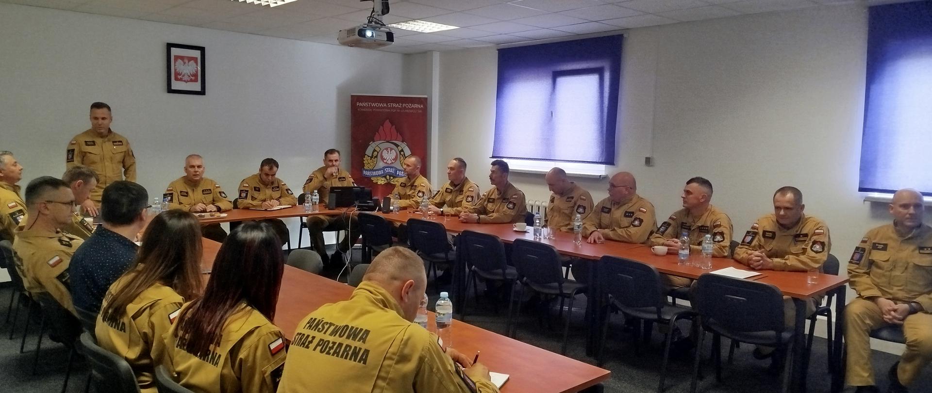 Grupa strażaków na sali konferencyjnej, przemawia Komendant Powiatowy PSP