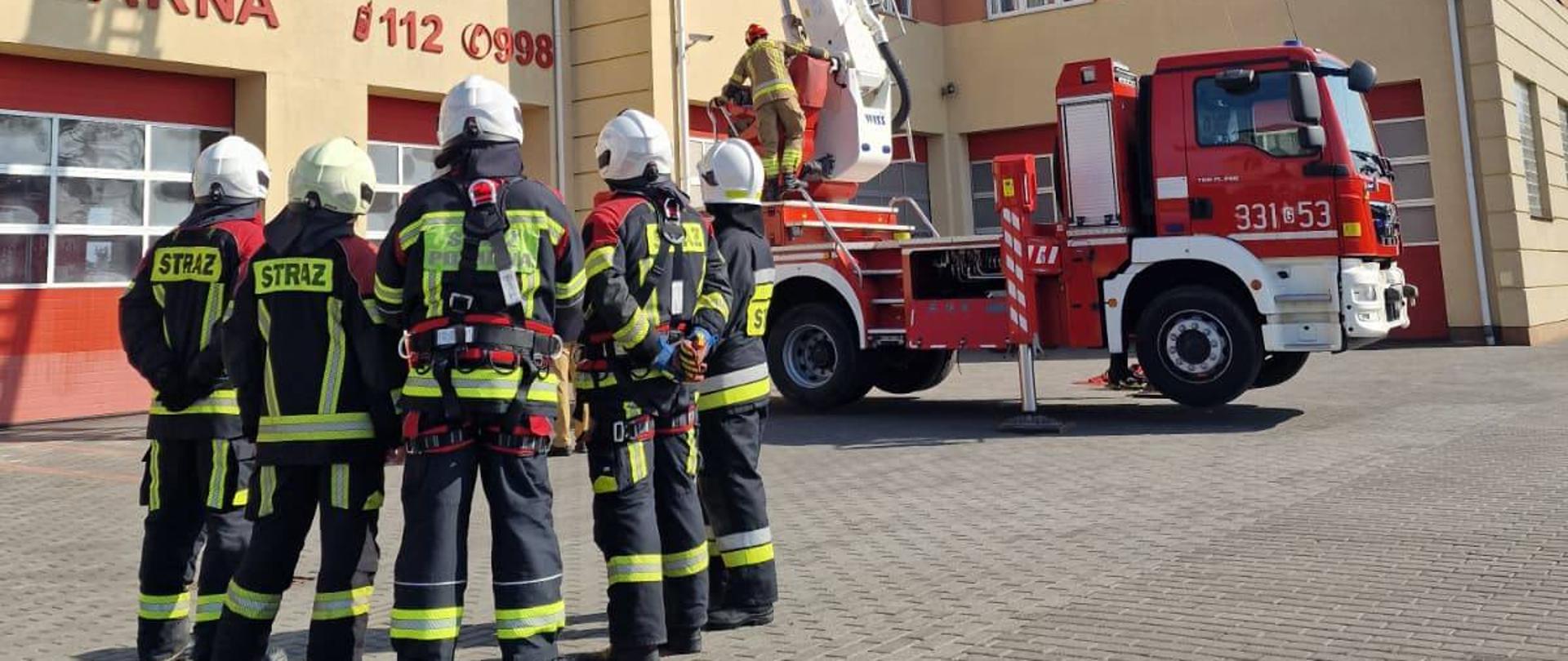 Na zdjęciu widzimy grupę strażaków OSP w tle podnośnik hydrauliczny