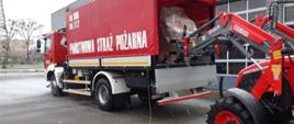 Zdjęcie przedstawiające ładowarkę, która rozładowuje środki do dezynfekcji z ciężarówki Państwowej Straży Pożarnej.