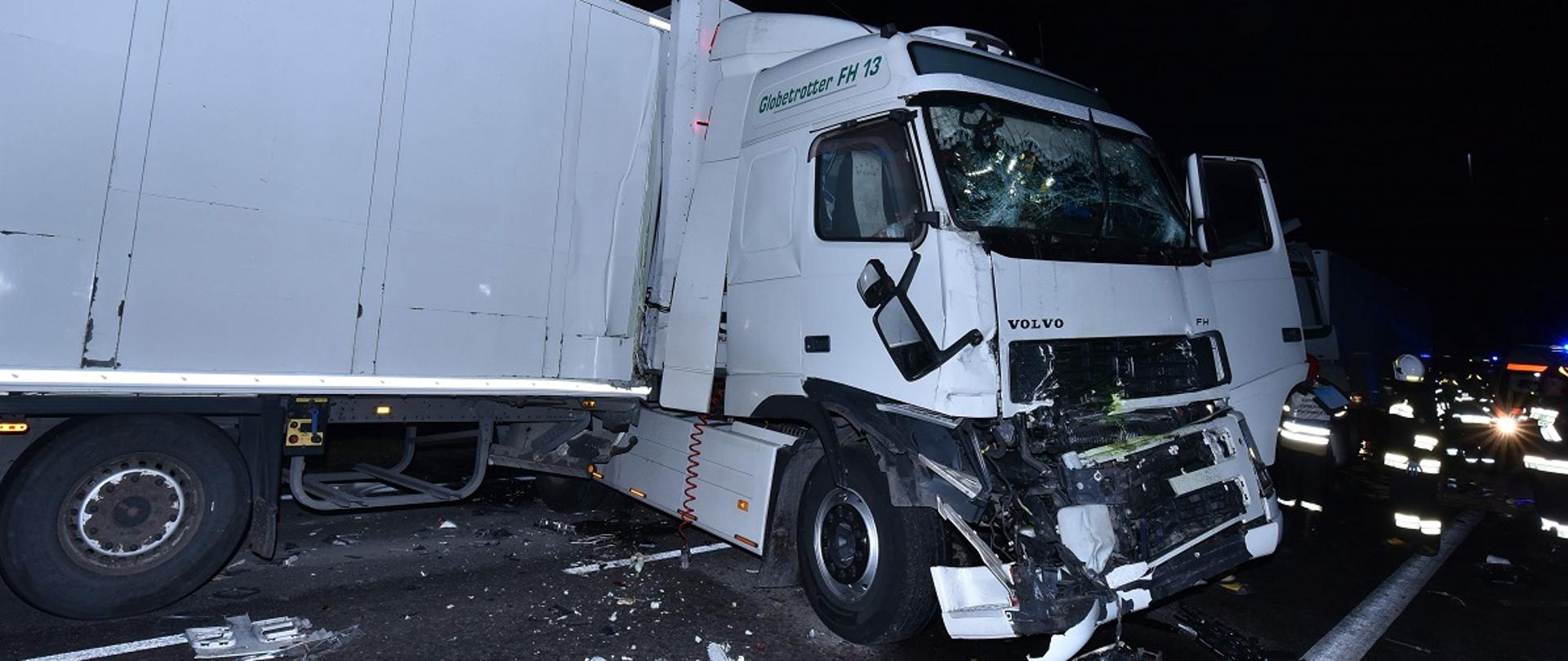 Uszkodzony samochód ciężarowy z lewej strony. Z prawej strony strażacy.