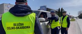 Funkcjonariusze w kamizelkach odblaskowych rozmawiają z osobą siedzącą w samochodzie.